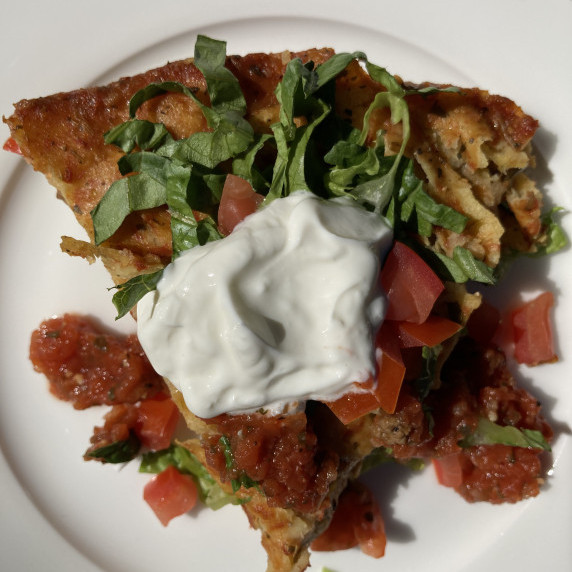 Slice of enchilada casserole topped with shredded lettuce, diced tomatoes and sour cream.