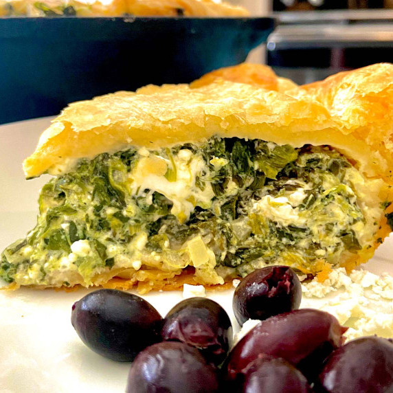 Slice of Spinach Feta Pie on white plate with kalamata olives.