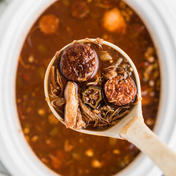 Overhead close up of a ladle of gumbo over a slow cooker.