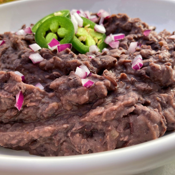 Refried black beans topped with jalapeño slices and diced red onion in a white bowl.