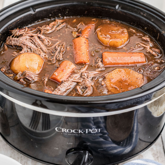 A crock pot full of venison roast with carrots and potatoes.