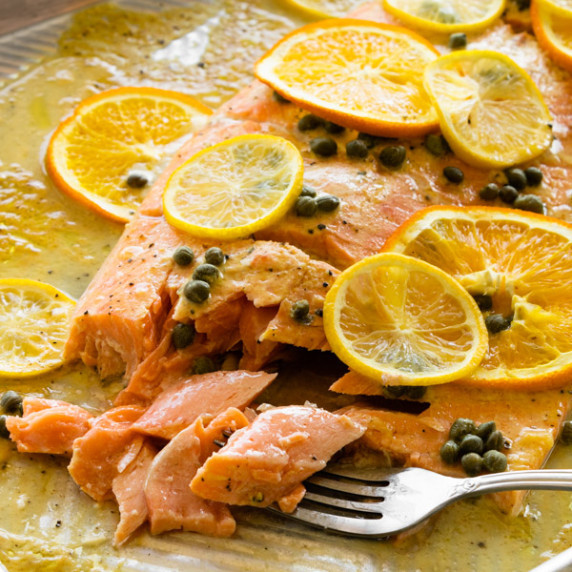 slow roasted salmon with citrus and capers on a baking sheet with a fork flaking salmon.