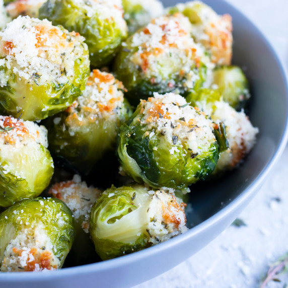 Smashed Brussels Sprouts RECIPE served in a white bowl topped with Parmesan cheese.