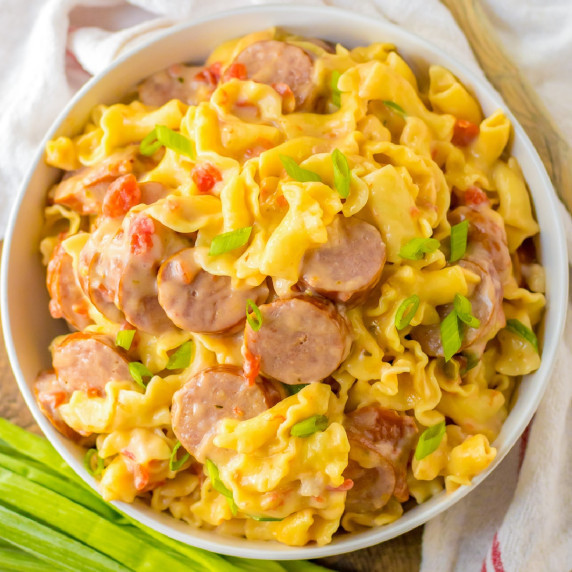 A bowl of smoked sausage pasta in a cheesy sauce topped with green onions.