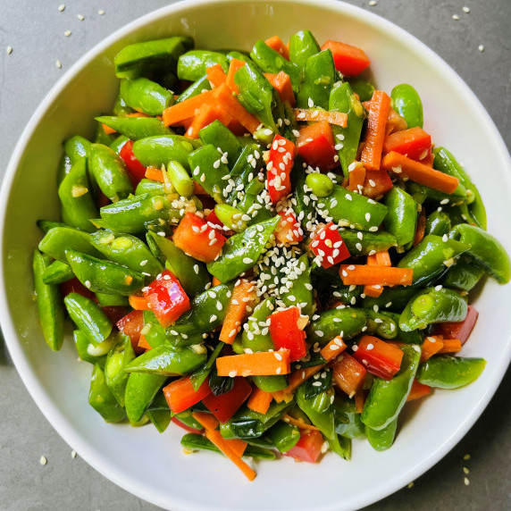 Salad made with snap peas, red pepper, carrots and onion in a ginger dressing in a white bowl.