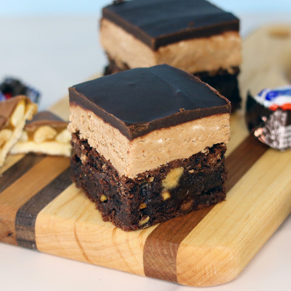 Snickers brownies on a wooden board with Snickers candy bars