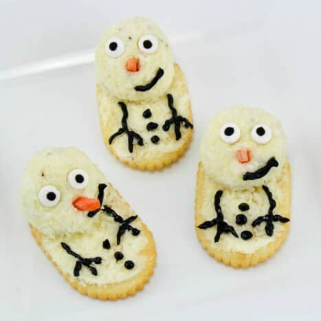 Three snowman cheese balls on oval crackers.