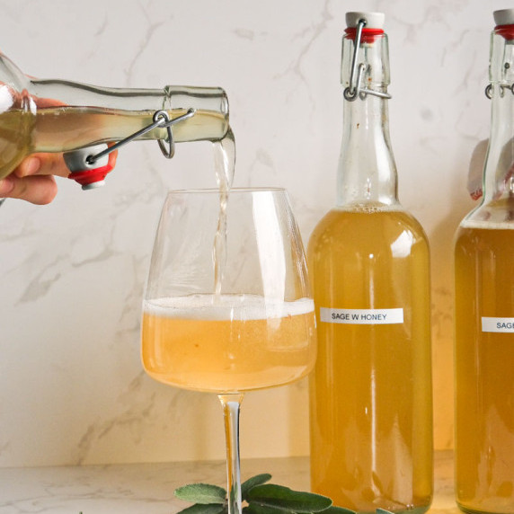 Someone poring sage kombucha in a glass