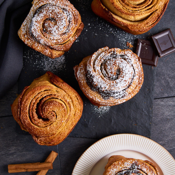 Two kinds of flaky Sourdough Brioche Feuilletee on slate, surrounded by chocolate and cinnamon