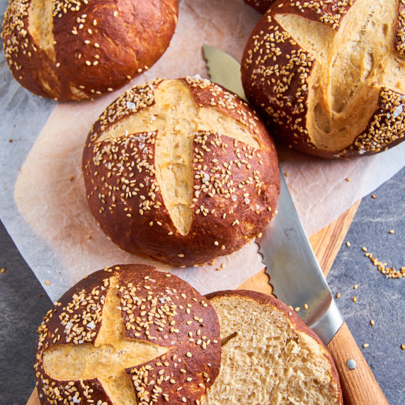 Fresh Sourdough Brioche Pretzel Buns on baking parchment, sprinkled with sesame and salt.