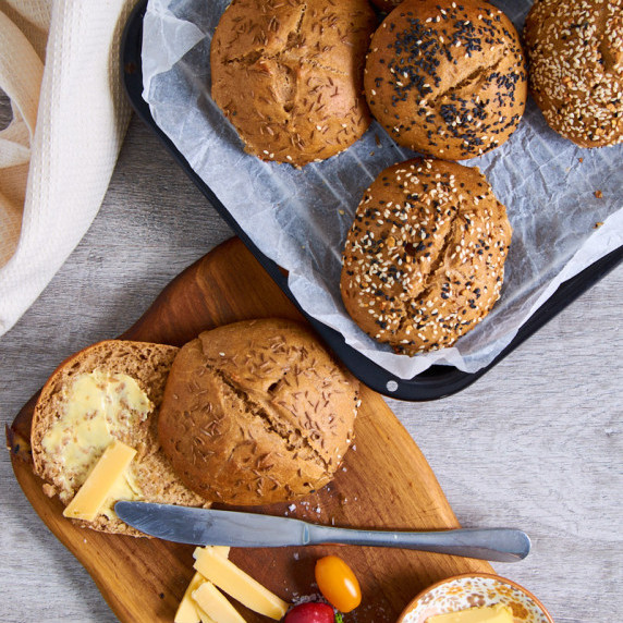 Soft and fluffy Rye Sourdough Rolls, one cut open with butter on top, beside it cheese and tomatoes.