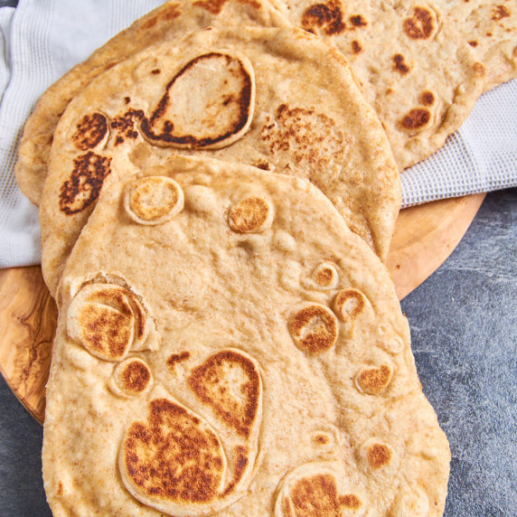 A stack of fresh soft and fluffy Sourdough Discard Naan on a board with a white kitchen towel