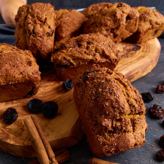 Mini Sourdough Pumpkin Soda Breads with Protein on a board, surrounded by raisins and cinnamon stick