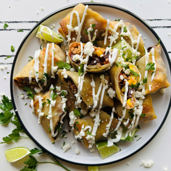 Southwest egg roll halves on a white plate topped with sour cream, cheese crumbles and cilantro.