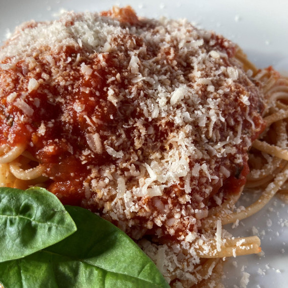 Spaghetti marinara garnished with fresh basil on a white plate.