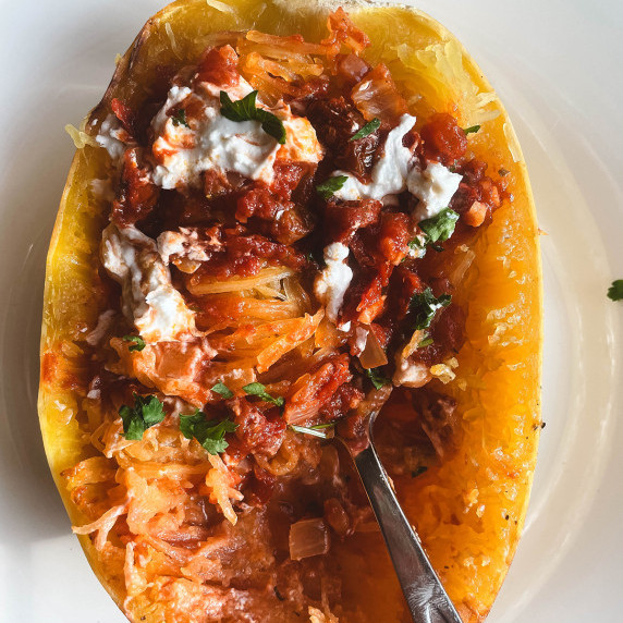 Half of a cooked spaghetti squash with tomato sauce and goat cheese crumbled on top.