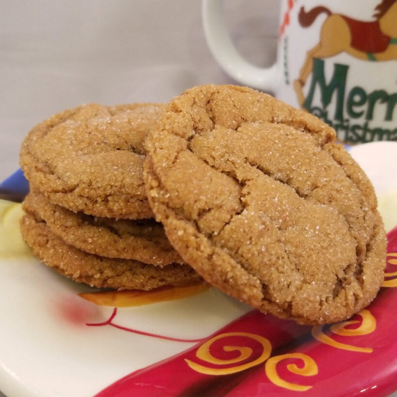 Spiced molasses cookies piled on a Christmas plate with a Christmas mug in the background.