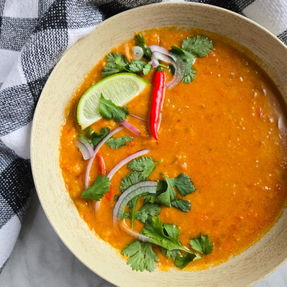 Bring orange soup with green and red garnishes against a checkered towel.