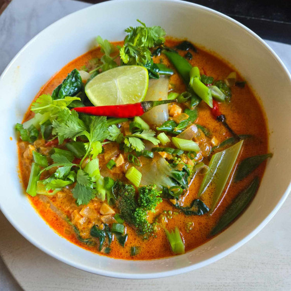 A bright red curry coconut broth with fresh, green veggies and herbs along with Red chili and lime