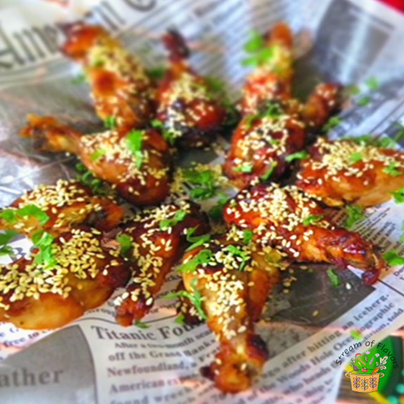 Spicy Honey-Glazed Chicken Wings topped with cilantro and toasted sesame seeds in newspaper