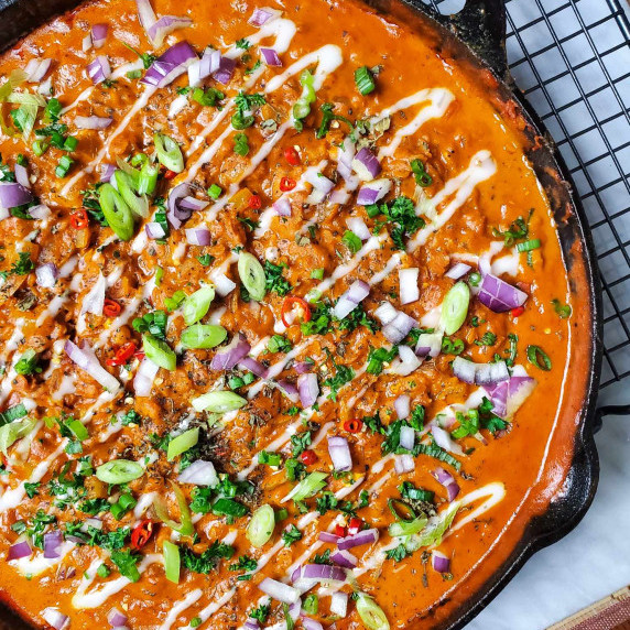a large skillet full of creamy, red lentils, garnished with a colourful assortment of toppings.
