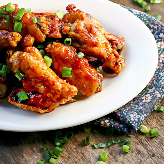 White plate full of spicy Thai Wings topped with chopped green spring onions