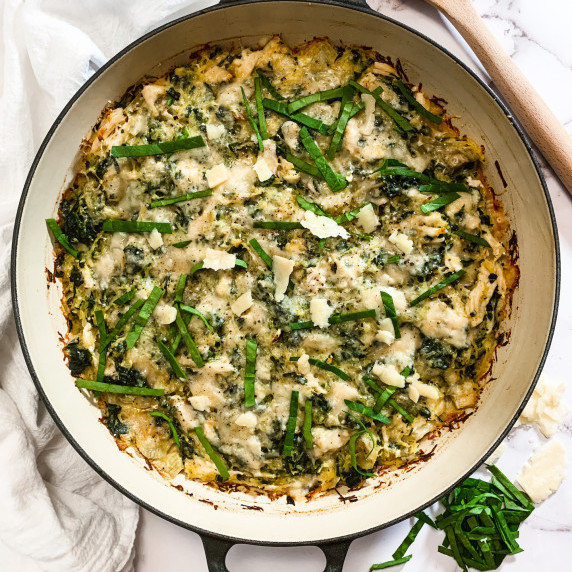 Enamel skillet with spinach artichoke casserole topped with spinach and parmesan crumbles