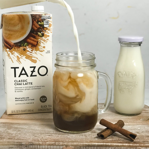 White milk is poured into a mason glass of dark brown chai concentrate, creating beautiful swirls.