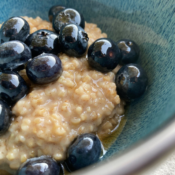 Steel cut oatmeal in a blue bowl topped with fresh blueberries and maple syrup.