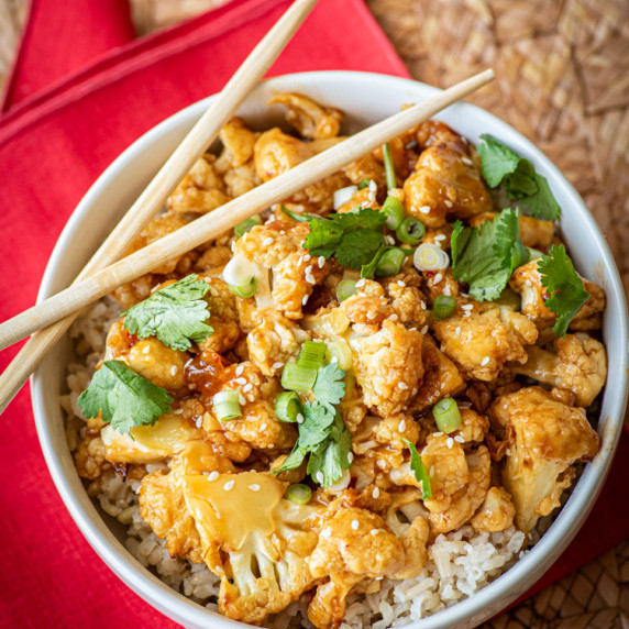 A bowl of sticky sesame cauliflower over rice with chopsticks.