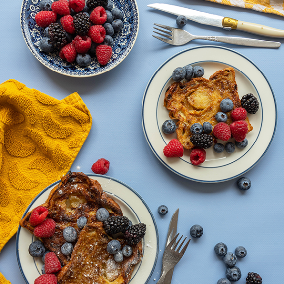 Three plates of stollen French toast with various red fruits on a blue backdrop.