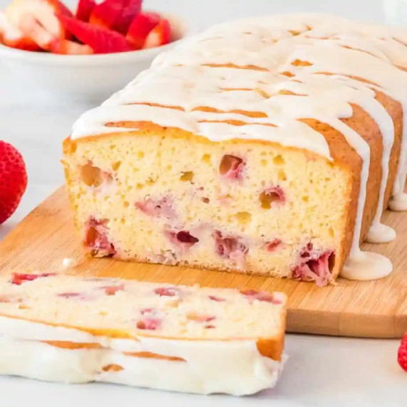 Close up of the inside of a slice of strawberry bread topped with white glaze on a cutting board.
