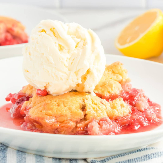 Close up view of the side of a plate with strawberry cobbler and a scoop of vanilla ice cream on top