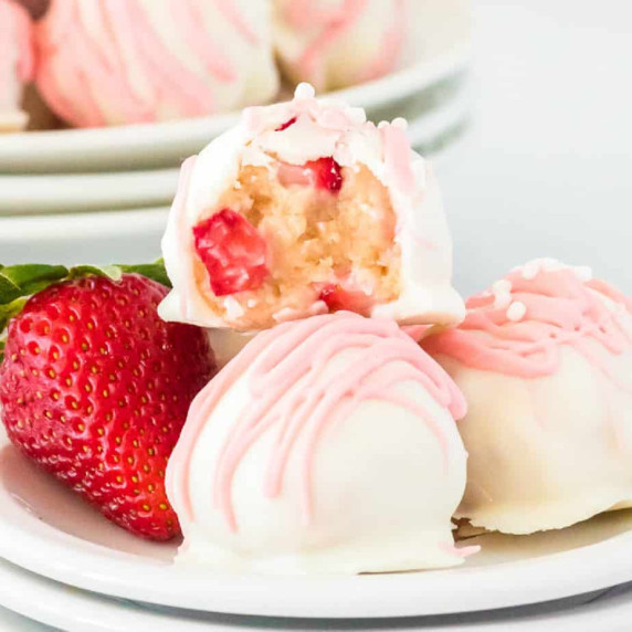 Close up of a strawberry shortcake truffle missing a bite showing strawberry bits inside.