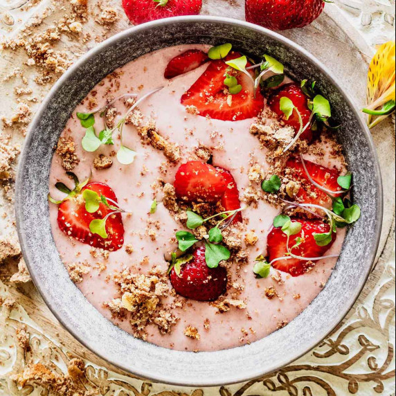 Strawberry banana smoothie bowl topped with fresh strawberries, micro greens, and crumble.