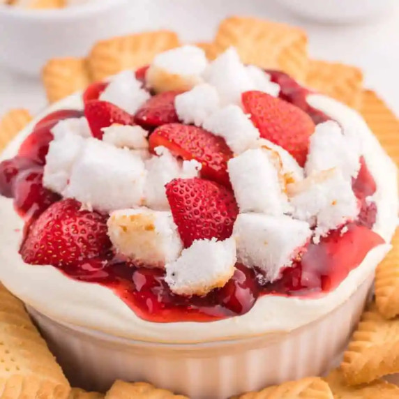 Cheesecake dip topped with strawberries, strawberry pie filling & angel food cake in a serving bowl.