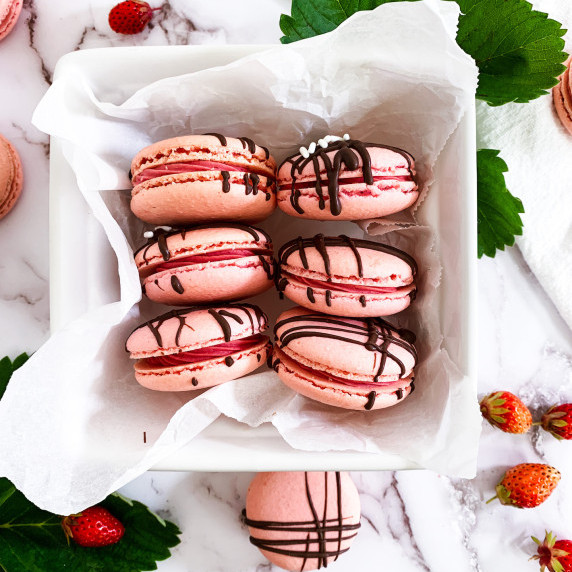 strawberry cheesecake macarons in a berry basket surrounded by strawberry leaves and berries