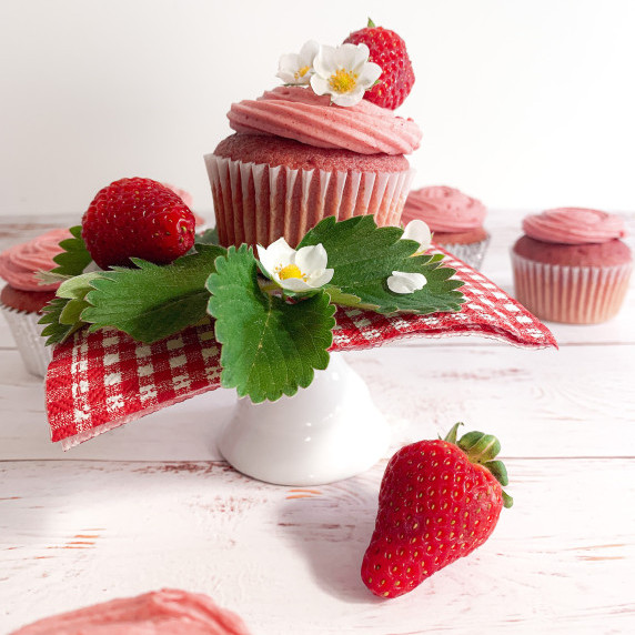 Frosted Strawberry Cupcake on a red gingham napkin on a whitewashed wood counter