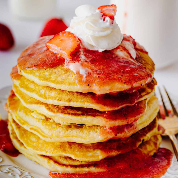Stack of strawberry pancakes topped with strawberry compote and whipped cream on a white plate
