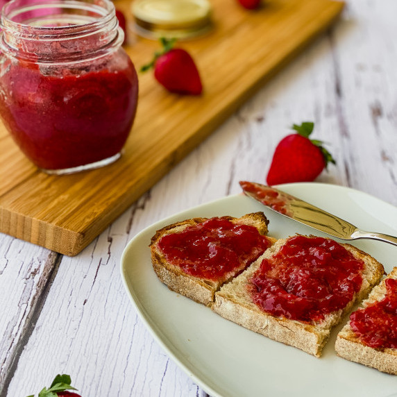 Strawberry Rhubarb Jam on a toast with a jar in the background.