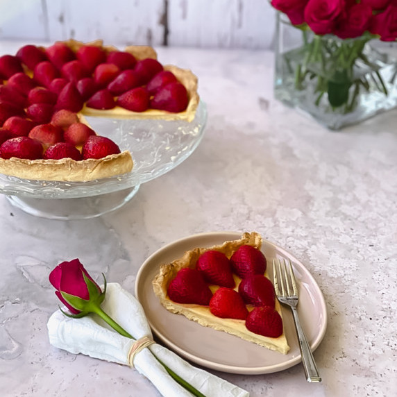 Slice of pie on plate with pie and flowers in the background.