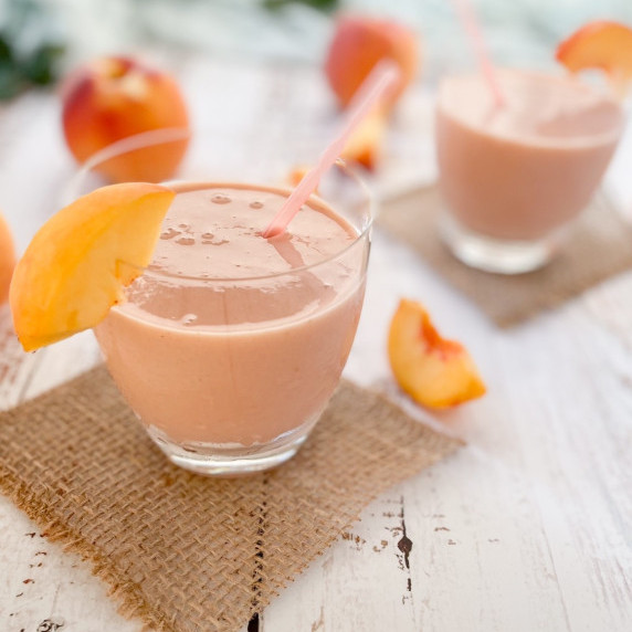 Strawberry peach smoothie in a glass with a straw and a slice of peach on the rim