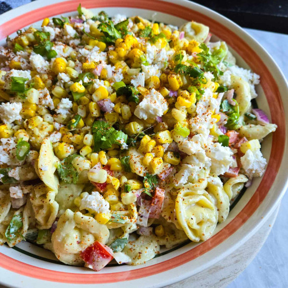 A colourful pasta salad with pops of yellow corn, green herbs, and white feta cheese