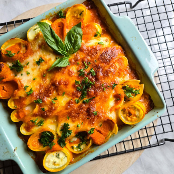 A blue baking dish filled with stuffed pasta, red sauce, and golden brown cheese.