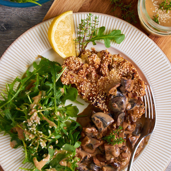 A plate of Sumac Roasted Cauliflower Steaks with Black Garlic Mushroom Sauce with arugula salad