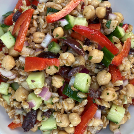 Grain salad with farro, chickpeas, cucumber, red pepper and onion in a white bowl. 