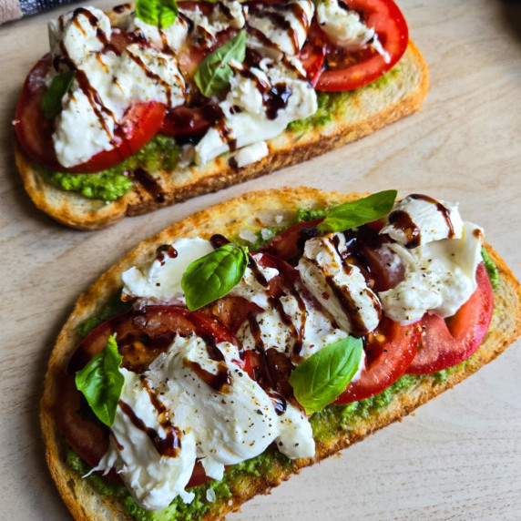 Golden toast topped with green pesto, red tomatoes, white burrata, black balsamic and basil