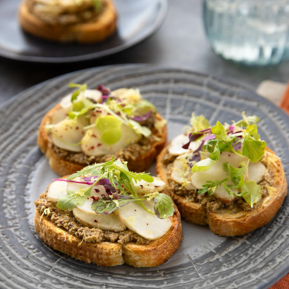 A plate with three pieces of toasted bread topped with tapenade and raw sunchoke slices.