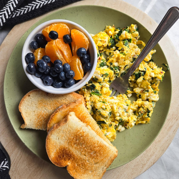 A green plate with golden toast, colourful fruit, and a yellow egg scramble.