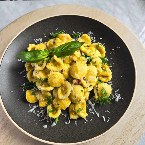 A vibrant yellow orecchiette on a matte black plate with fresh green herbs